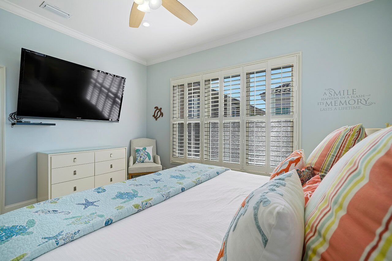 A bedroom with a bed, a TV, a dresser, a chair, and a window with shutters.