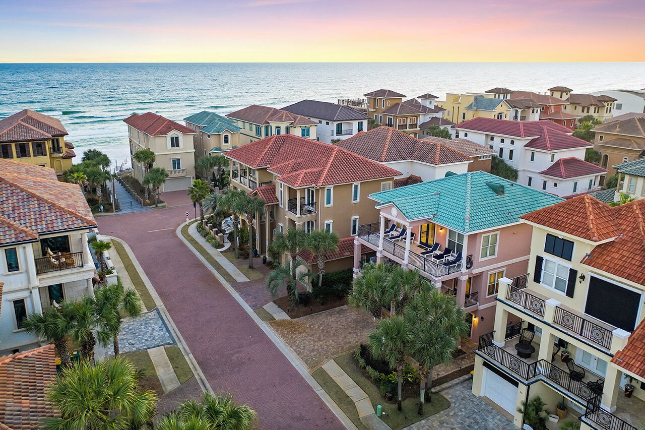 A coastal residential area with houses featuring red-tiled roofs, balconies, and a paved street.