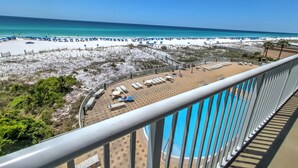 A beach view from a balcony with a pool, lounge chairs, and umbrellas.