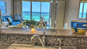 A kitchen with granite countertops, stainless steel sinks, and a view of the ocean through large windows.