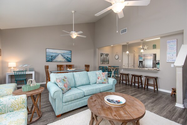 A modern living room with a light blue sofa, wooden coffee table, and a dining area with bar stools. - Family Getaway | Heated Pool, Patio & Play Area (Corpus Christi)
