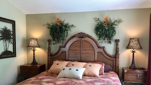 Una cama con colcha estampada, dos mesitas de noche con lámparas y plantas decorativas en la pared.