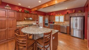 A spacious kitchen with wooden cabinets, granite countertops, and a central island with chairs. - Spacious Mountain Escape w/ Hot Tub and Fireplace (OAKLAND)