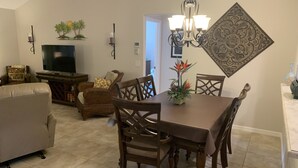 A dining area with a brown table, four chairs, a chandelier, and a decorative wall piece. - Beautiful 3/2 Sm Dog Friendy home w/WiFi! Central Location to each town! (The Villages)