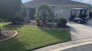 A residential house with a garage, a well-maintained lawn, and a golf cart parked in front. - Beautiful 3/2 Sm Dog Friendy home w/WiFi! Central Location to each town! (The Villages)