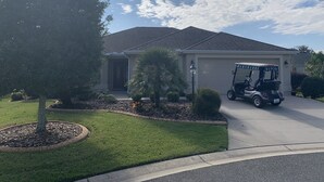 A residential house with a garage, a lawn, and a golf cart parked in front. - Beautiful 3/2 Sm Dog Friendy home w/WiFi! Central Location to each town! (The Villages)