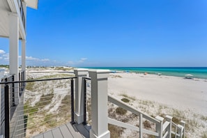 A beach view from a balcony with a railing, sandy beach, and ocean.