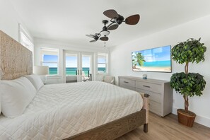 Een slaapkamer met een bed, een plafondventilator, een televisie, een plant en uitzicht op de oceaan.