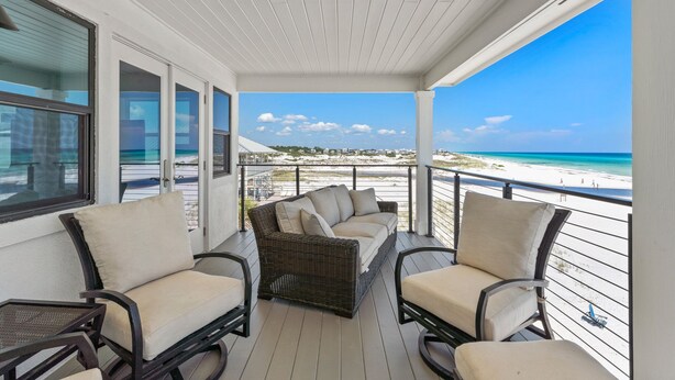 Een overdekt balkon met rieten meubilair en uitzicht op het strand, onder een heldere lucht.