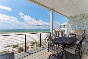 Een overdekt buitengebied met een tafel, stoelen, een barbecue en uitzicht op het strand.