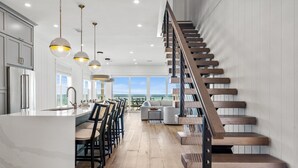 Een moderne keuken met een centraal eiland, een houten trap en grote ramen met uitzicht.