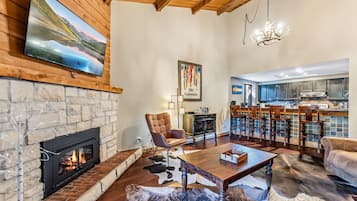 Una sala de estar con chimenea, televisión y una cocina al fondo.