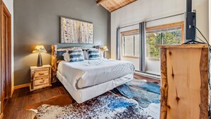 Un dormitorio con cama, mesita de noche, lámpara, cuadro, ventana y televisor.