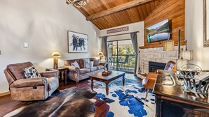 Un salón amplio con chimenea, muebles de cuero, una alfombra grande y vistas panorámicas.