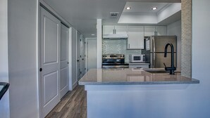 A modern kitchen with white cabinetry, a stainless steel refrigerator, a microwave, and a black faucet. - Free Beach Service Canal Views! Pet Friendly! Sandpiper Cove 4103! (Destin)