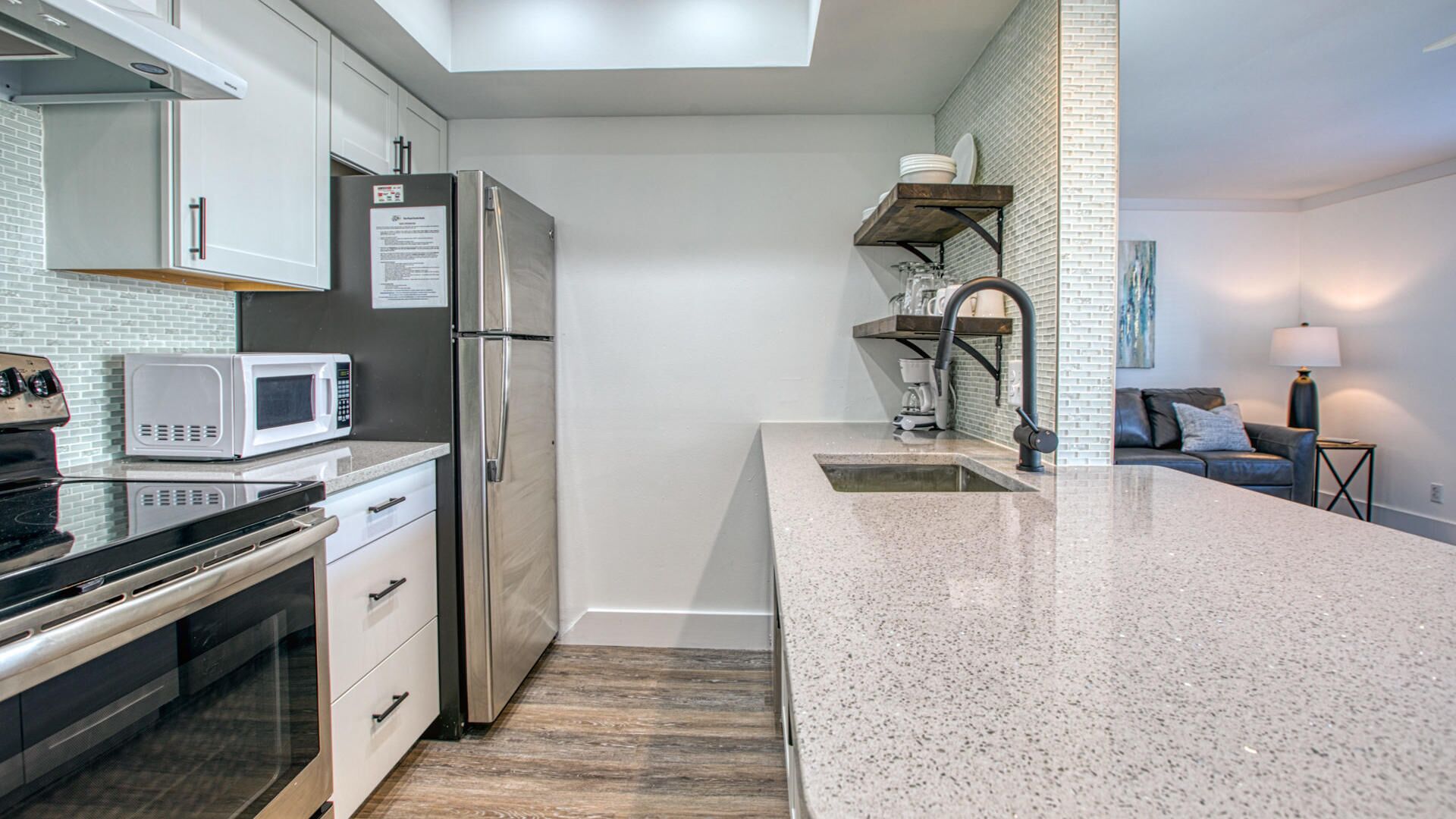 A modern kitchen with a stainless steel refrigerator, a microwave, and a built-in oven. There is a granite countertop and a sink with a modern faucet.