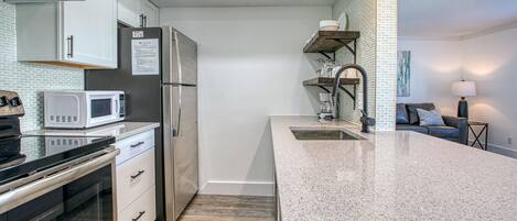 A modern kitchen with a stainless steel refrigerator, a microwave, and a built-in oven. There is a granite countertop and a sink with a modern faucet.