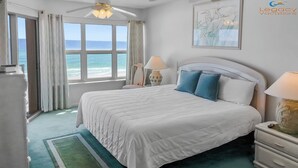 A bedroom with a bed, a nightstand, a lamp, a window with curtains, a ceiling fan, and a framed picture on the wall. - Budget Friendly 2Bd Beachfront with $1000000 View! Seasonal Beach Service! (Fort Walton Beach)