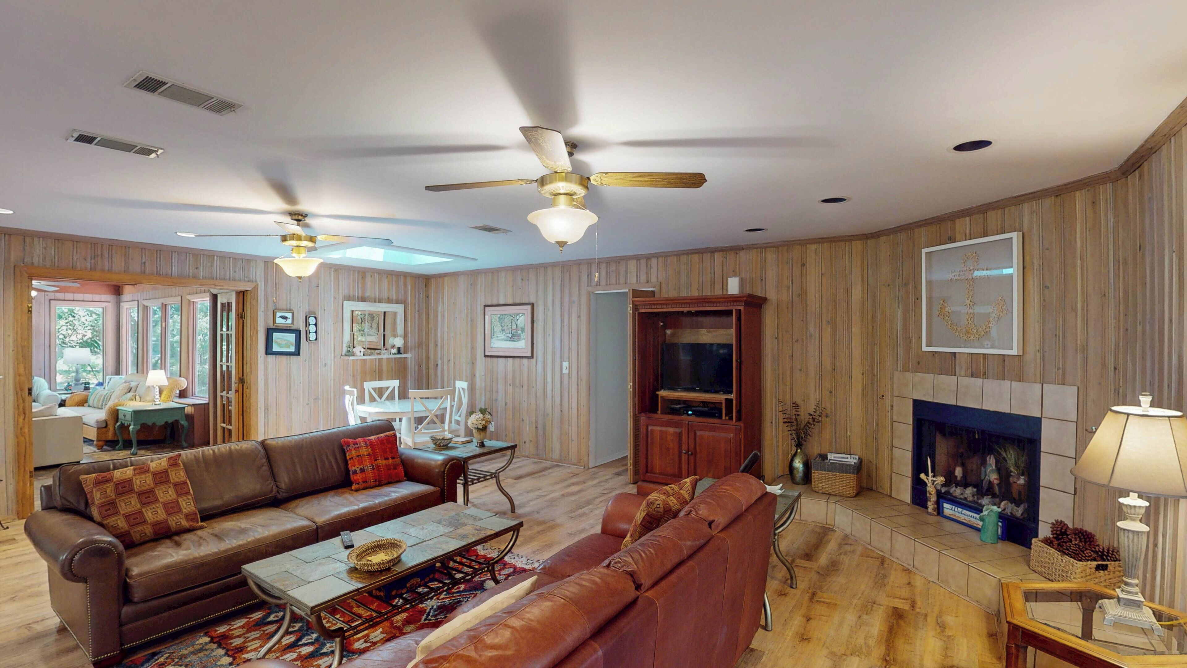 A spacious living room with a fireplace, wooden paneling, and ceiling fans.