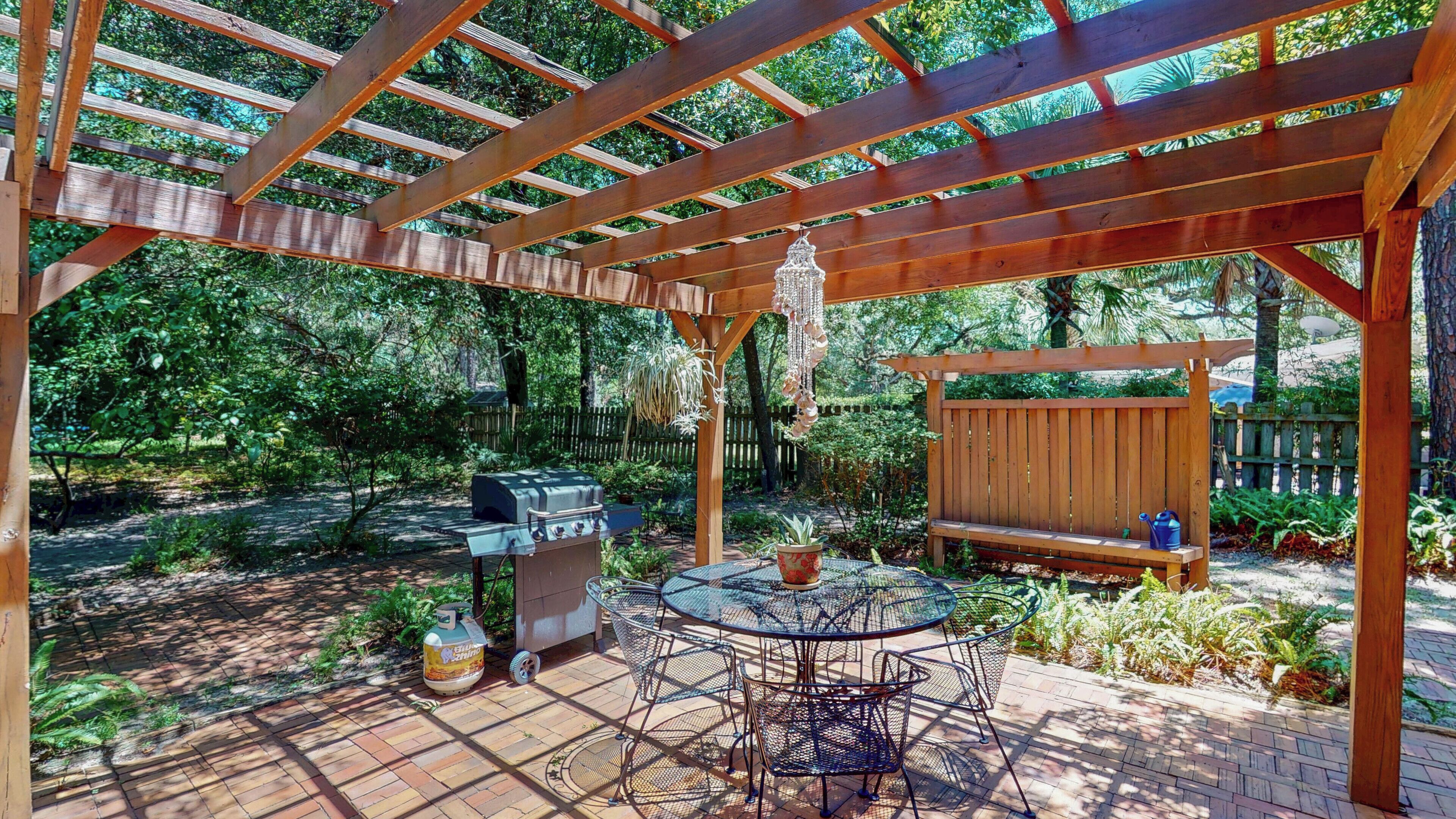 A covered patio area with a grill, a table with chairs, and a wooden bench.