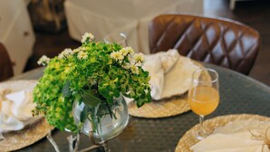 Una mesa de comedor dispuesta con posavasos de mimbre, servilletas blancas y un florero de vidrio con flores.