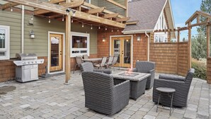 Une terrasse extérieure aménagée avec des meubles en osier, un barbecue et des guirlandes lumineuses.