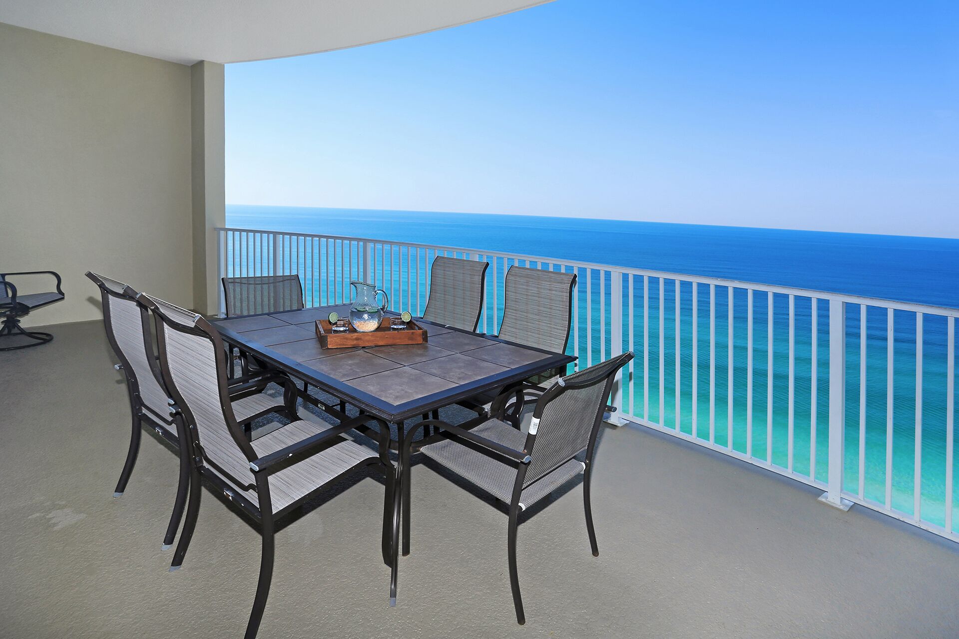A balcony with a table and chairs, overlooking a clear blue ocean.