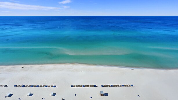 A beach with rows of sun loungers and a clear view of the ocean.