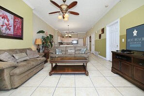 A living room with a brown sofa, a wooden coffee table, a ceiling fan, and a television on a wooden stand.