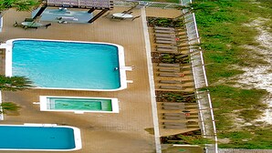 An aerial view of a resort with a large rectangular swimming pool, a smaller pool, and a covered seating area with tables and chairs.