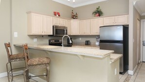 A kitchen with beige cabinetry, a central island with bar stools, a black refrigerator, a microwave, and a stove.