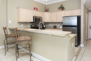 A kitchen with beige cabinetry, a central island with bar stools, a black refrigerator, a microwave, and a stove.