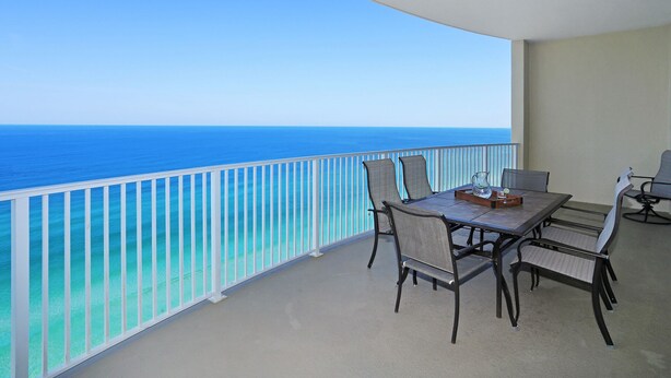 A balcony with a table and chairs, overlooking a clear blue sea.
