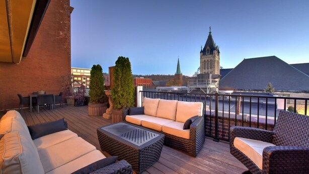 Eine Dachterrasse mit Gartenmöbeln, Blick auf eine Kirche und ein Backsteingebäude im Hintergrund.