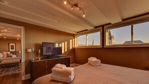 Ein Schlafzimmer mit einem großen Bett, einem Fernseher, einer Kommode und einem Fenster mit Blick auf ein Gebäude.