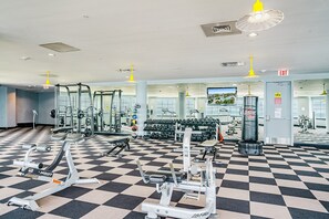 Une salle de sport équipée de divers appareils d’exercice, dotée d’un sol à carreaux et d’un grand miroir.