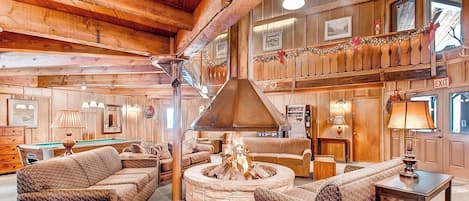 A cozy, rustic interior with a stone fireplace, wooden beams, and a billiards table.