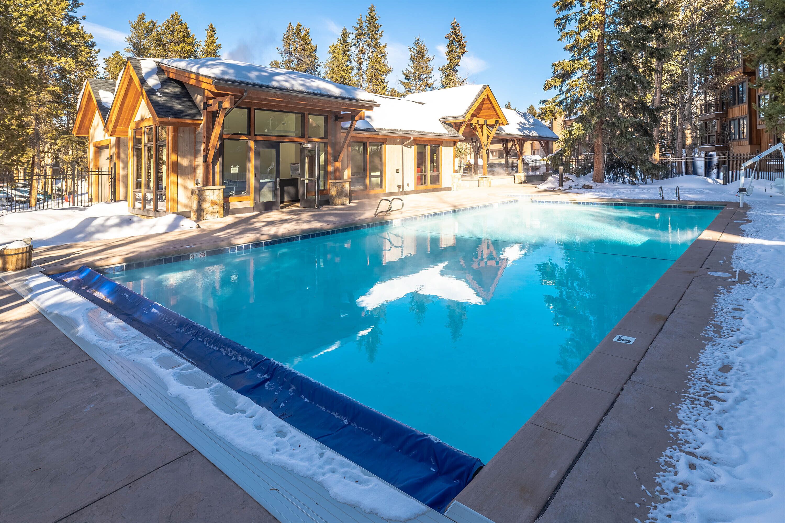 Un área de piscina con cabañas de madera, rodeada de nieve y árboles.