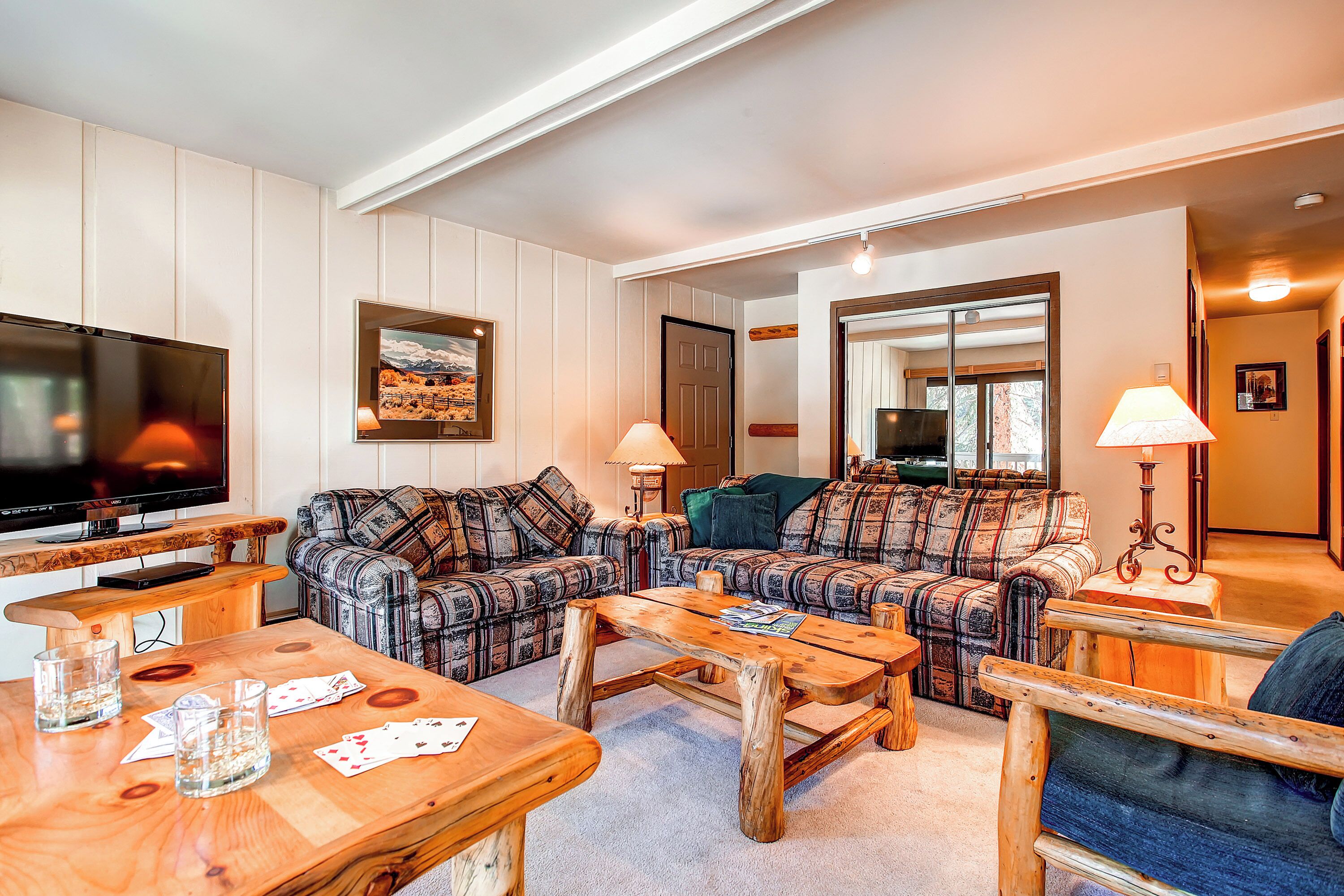 A living room with a TV, two sofas, a coffee table, and a dining table with cards and glasses.