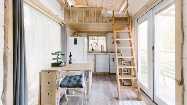 A compact kitchen with a wooden ladder, a dining area with a table and chairs, and a small potted plant. - Modern Cozy Urban Tiny House near Airport and Transportation-Private Setting (Des Moines)