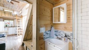 A wooden cabin interior with a kitchen, a bathroom with a white sink and mirror, and a wooden staircase. - Modern Cozy Urban Tiny House near Airport and Transportation-Private Setting (Des Moines)