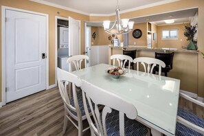 A dining area with a glass table, white chairs, and a chandelier.