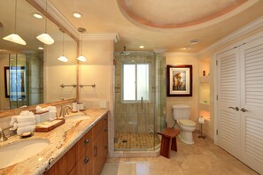 A bathroom with a glass-enclosed shower, a large mirror, and a vanity with a marble countertop.