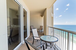 A balcony with a glass table and chairs, overlooking a beach.
