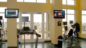 Un gimnasio con cintas de correr, bicicletas estáticas y una pantalla de televisión que muestra un noticiero.