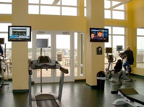 A gym with treadmills, stationary bikes, and a TV screen displaying a news channel.