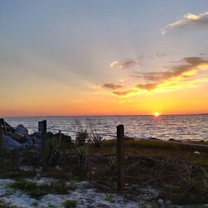 A sunset over a beach with a fence and rocks in the foreground.