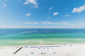 A beach with clear turquoise water, a sandy shore, and a row of blue umbrellas.