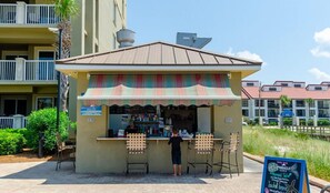 A small outdoor kiosk with a striped awning, two bar stools, and a person standing behind the counter.