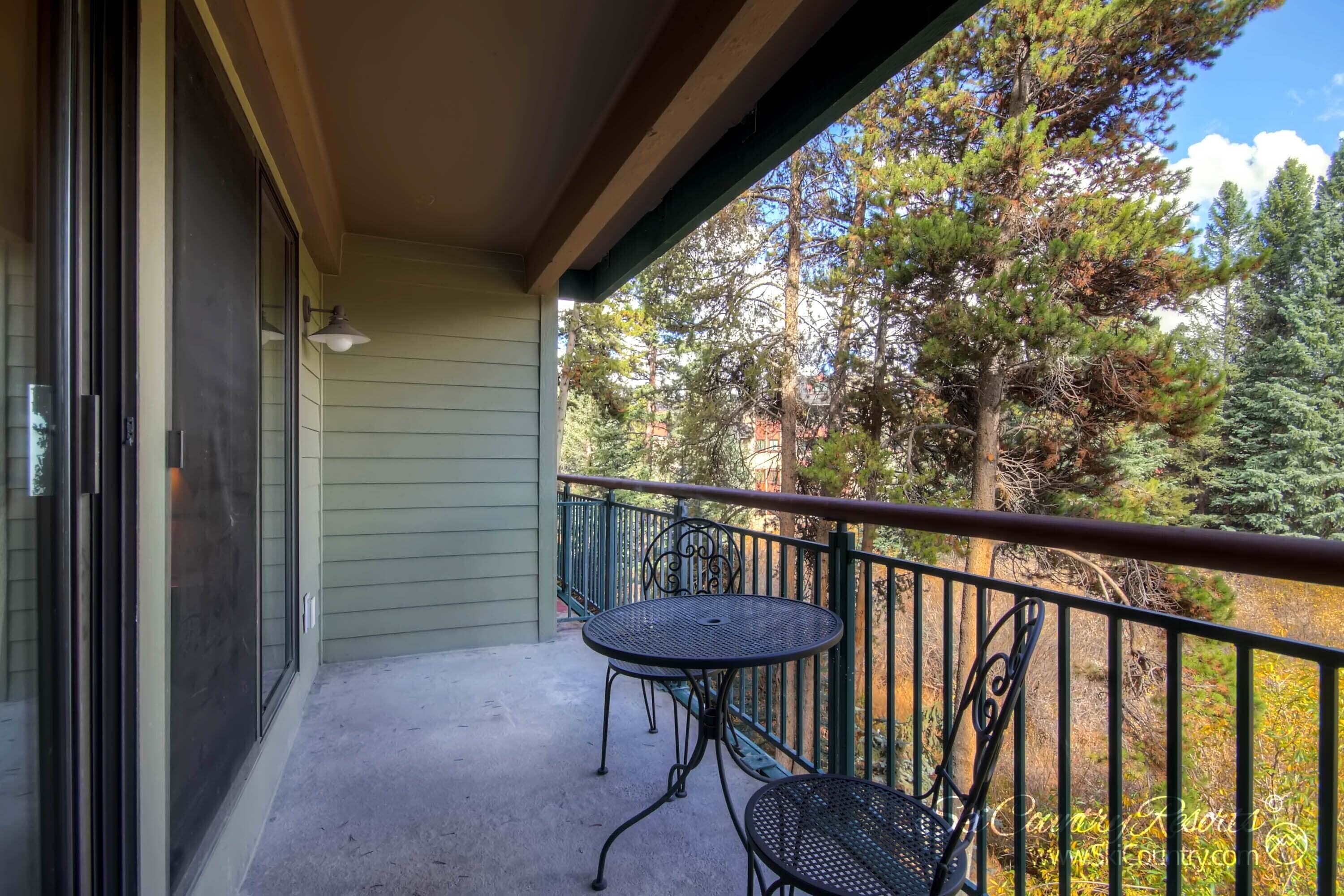A balcony with a table and chairs, overlooking a forested area.
